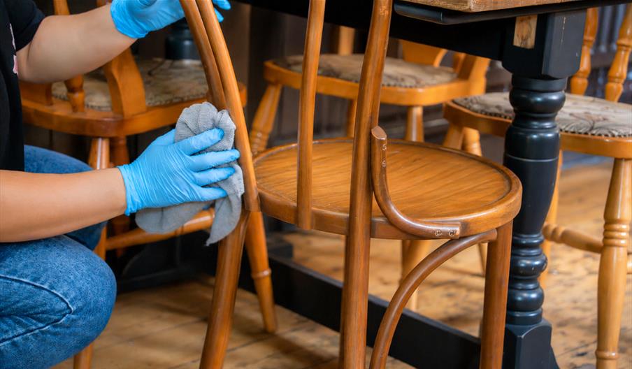 Someone cleaning wooden bar restaurant chairs with a cloth