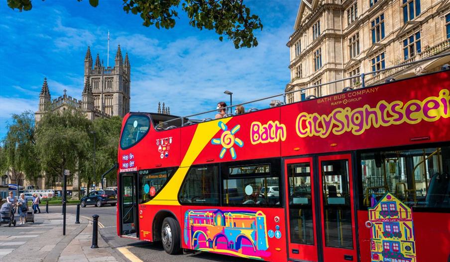 Red "Bath CitySightseeing" open-top bus with Bath Abbey visible in the background.
