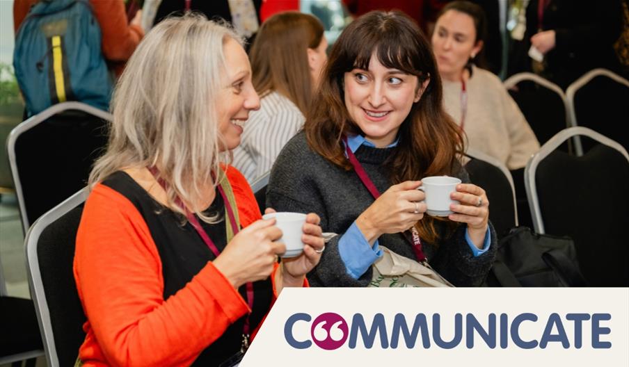 Two women sat down, smiling at each other while holding cups of tea. The "Communicate" conference logo is overlayed in the bottom right.
