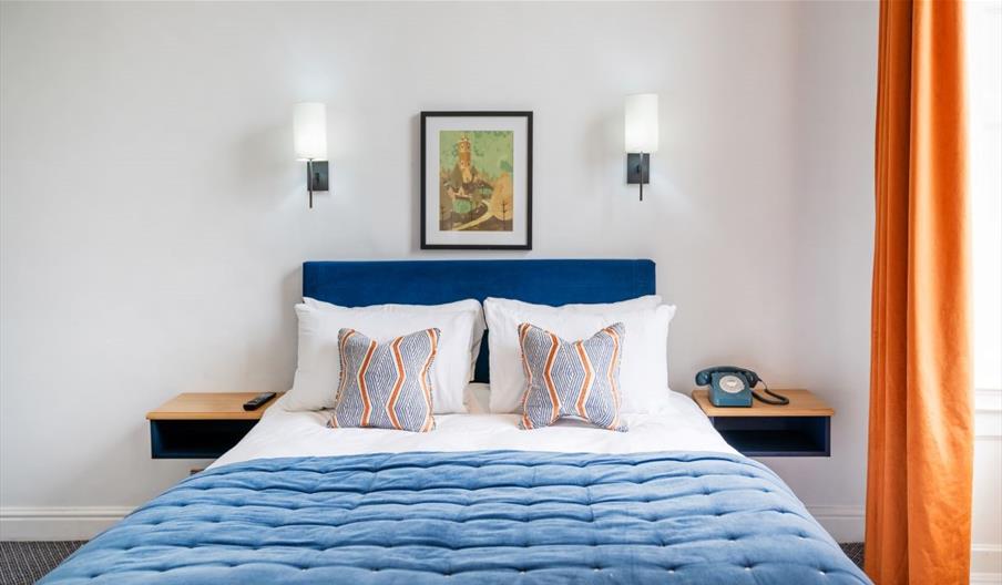 A twin-sized bed with blue and white sheets, alongside an orange curtain.