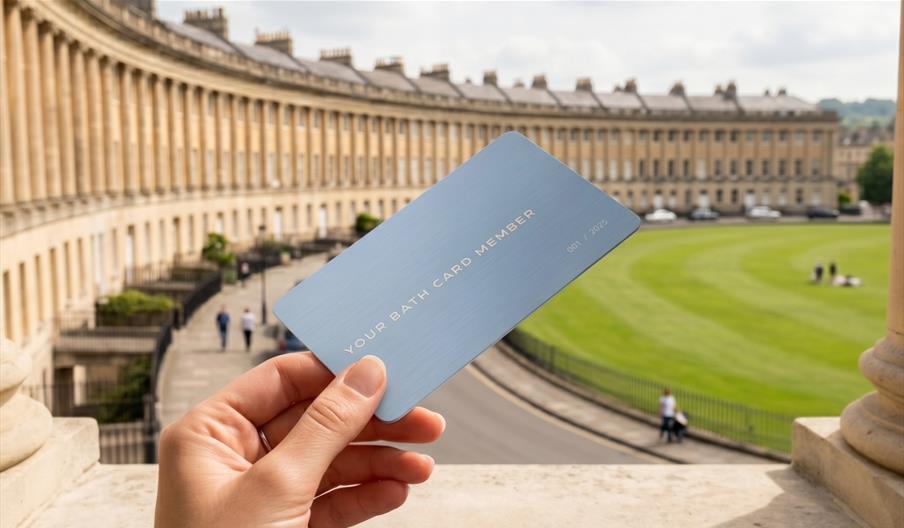 A close up of a hand holding a member card with the Royal Crescent in the background.