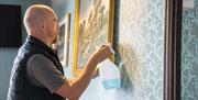 A man cleaning a painting on a wall holding a spray bottle