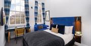 A double bed with blue headboard, in a room with white walls and grey carpet.