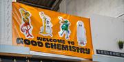 A large yellow vinyl sign hanging on a wall that says 'Welcome to Good Chemistry'