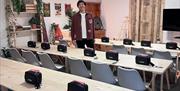 A man standing in a room with rows of tables with presentation boxes on in front of each chair.
