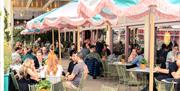 A large number of people seated in the outside dining area of Ritorno Lounge under pink and blue parasols.