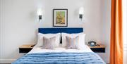 A twin-sized bed with blue and white sheets, alongside an orange curtain.