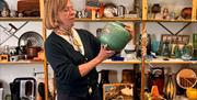 Person holding a vase in front of shelves of ceramics