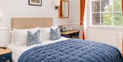 A double bed with blue and white sheets, alongside a large window with orange curtains.