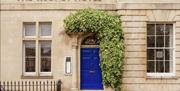 The exterior of The Rodney Hotel, with gold lettering and thick ivy above a blue door.