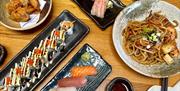 A birdseye shot of a selection of Japanese foods on plates, like sushi and noodles.